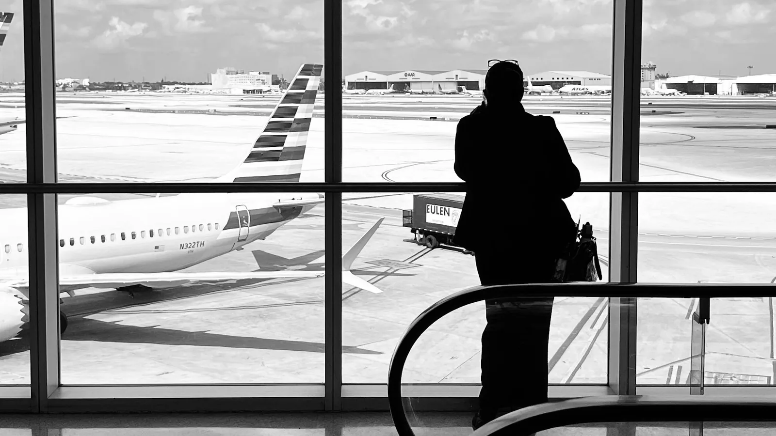 Silhouette d'un voyageur devant la baie vitrée d'un terminal aéroportuaire, mood de décision longue portée.