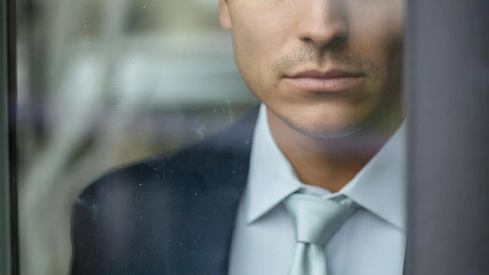 Homme en costume sombre regardant par une fenêtre, profil type de l'entrepreneur de 38-48 ans qui envisage un projet familial international.